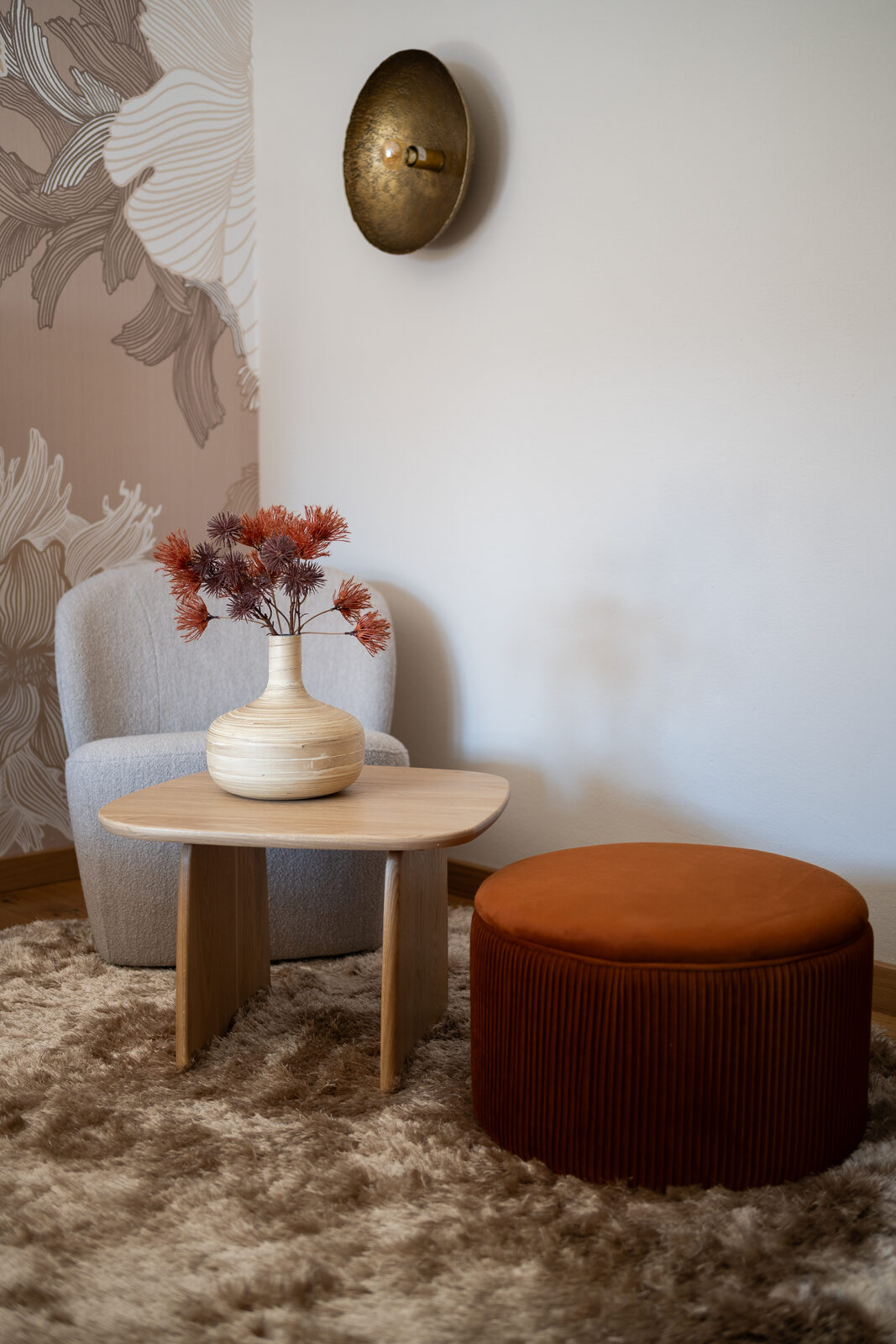 Sitting corner: grey velvet armchair, terra-cotta pouf, brass wall light.