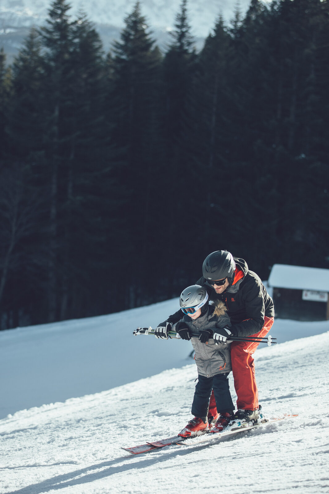 A parent teaches a child to ski on a quiet morning piste.